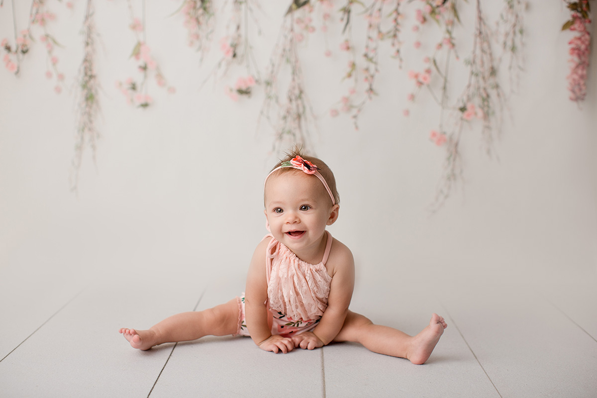A happy baby sits with legs out and a big smile in a studio wearing a pink floral outfit after visiting Calvary Day Care Springfield, IL