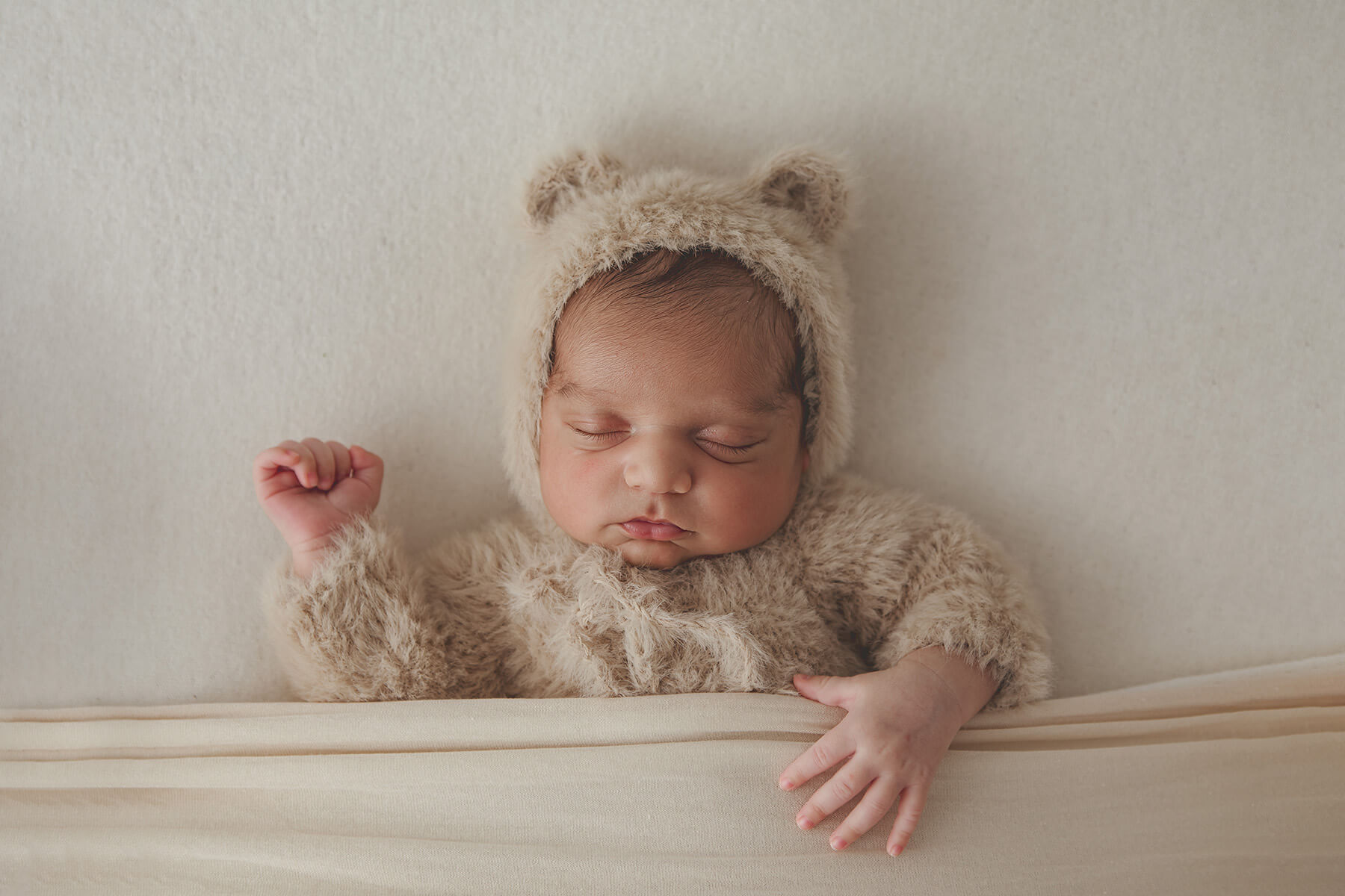 A newborn sleeps in a fur teddy onesie with hood and ears in a studio after some baby classes in springfield il