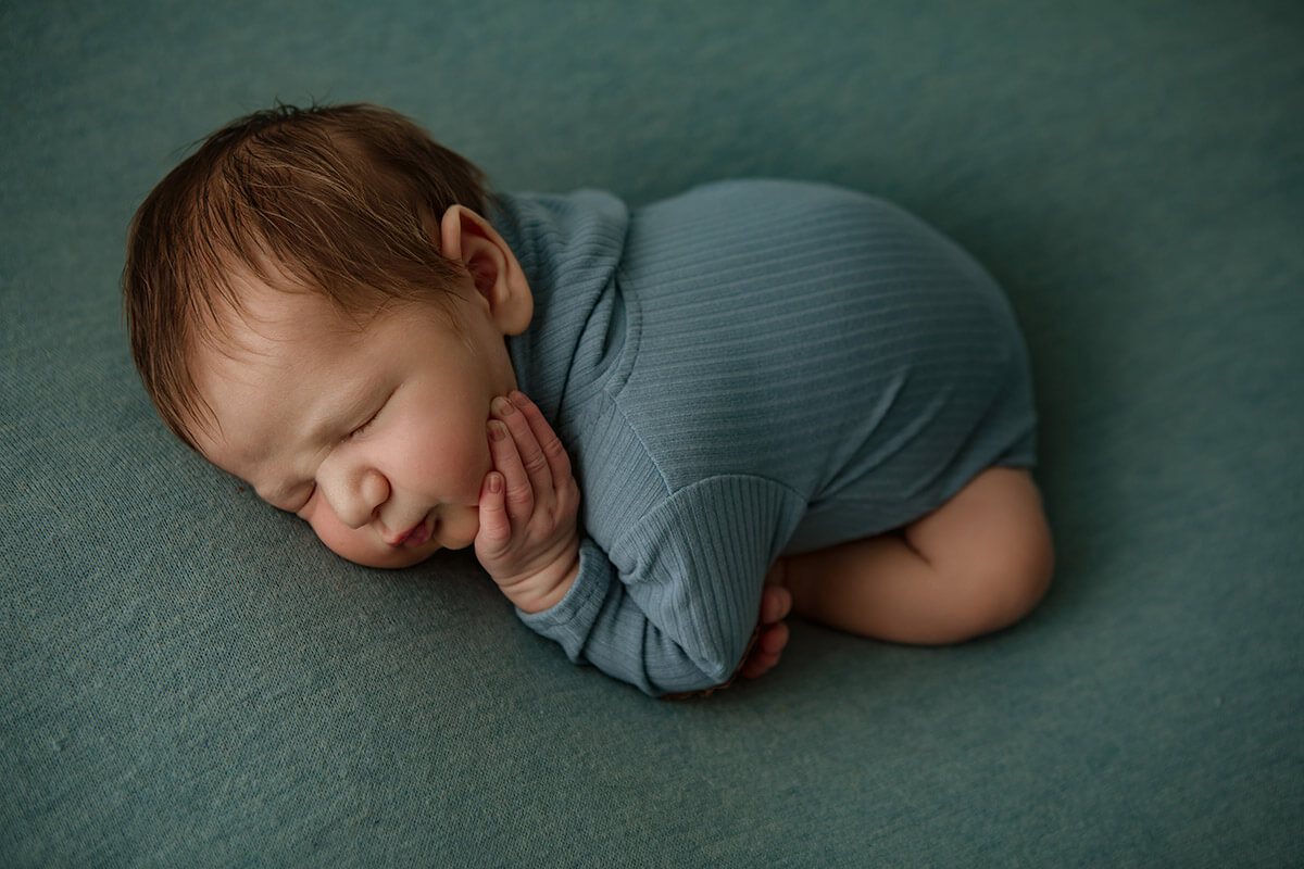 A newborn baby sleeps in a blue onesie on his tummy in a studio after some baby classes in springfield il