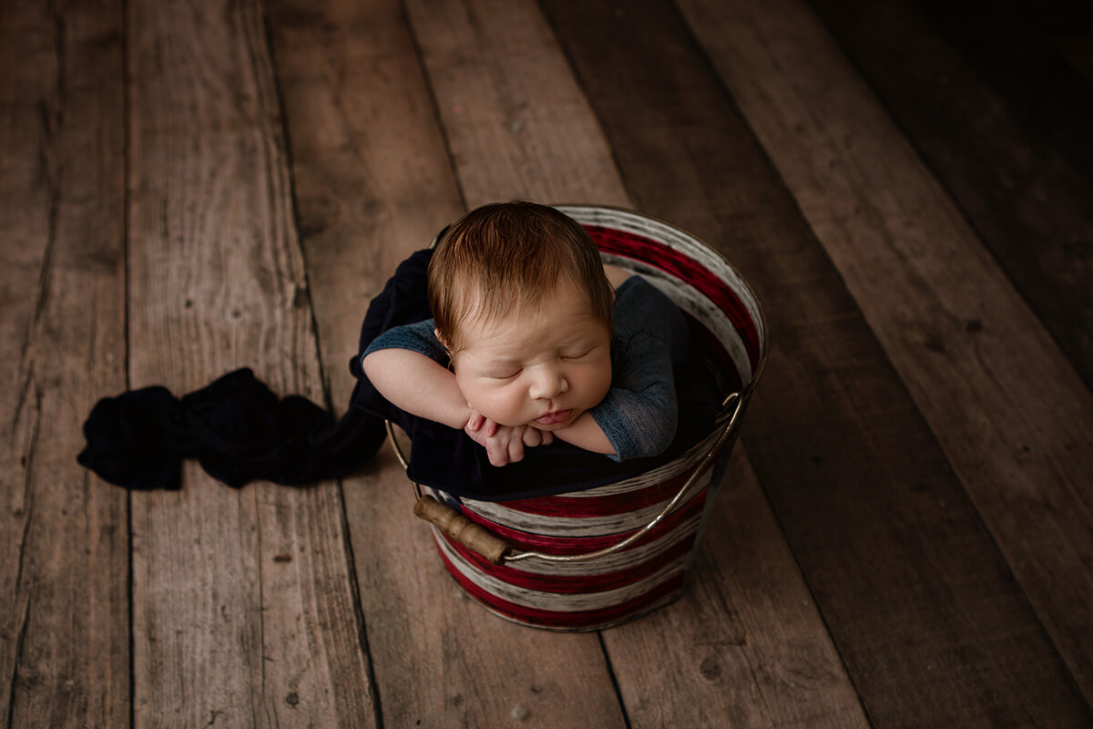 A baby sleeps in a metal bucket on wooden floor in a studio