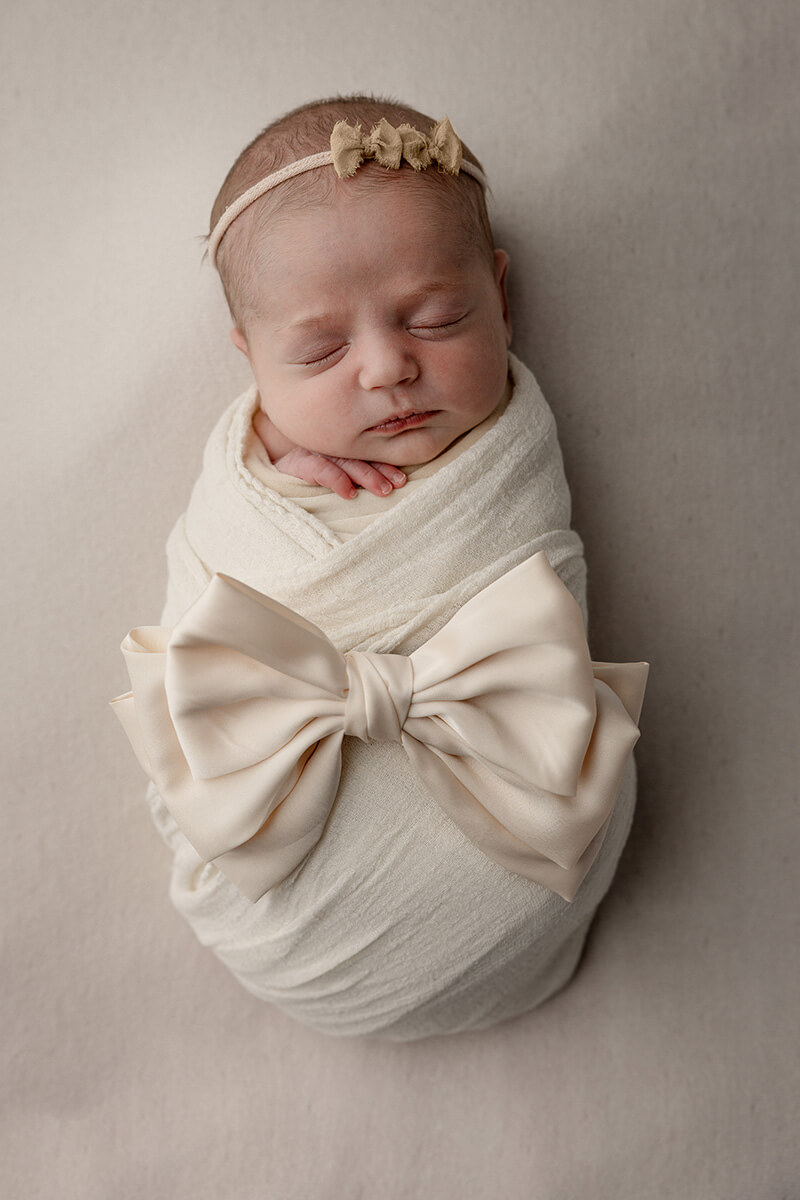 A newborn baby sleeps in a white swaddle with a bow in a studio after some baby classes in springfield il