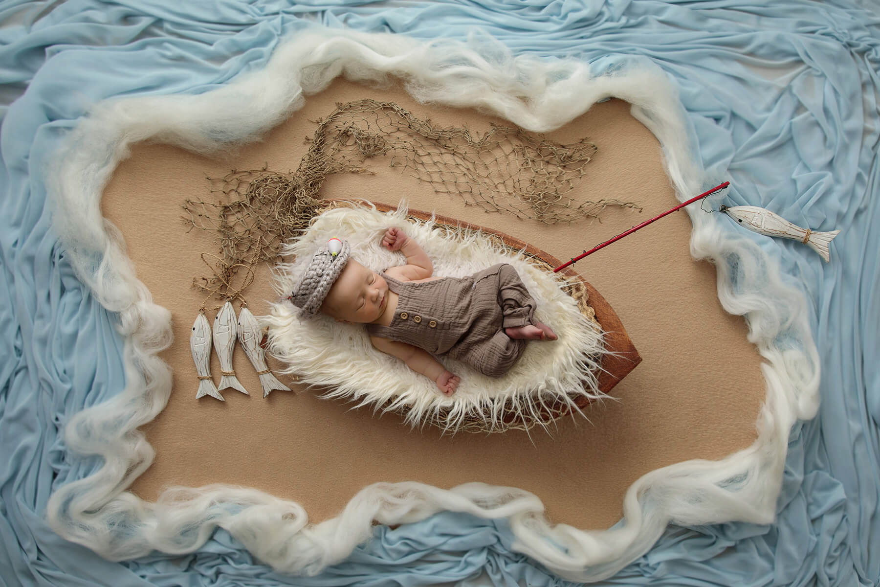 A newborn baby sleeps in a tiny boat with a river of fabric and wooden fish after some baby swim lessons in springfield il