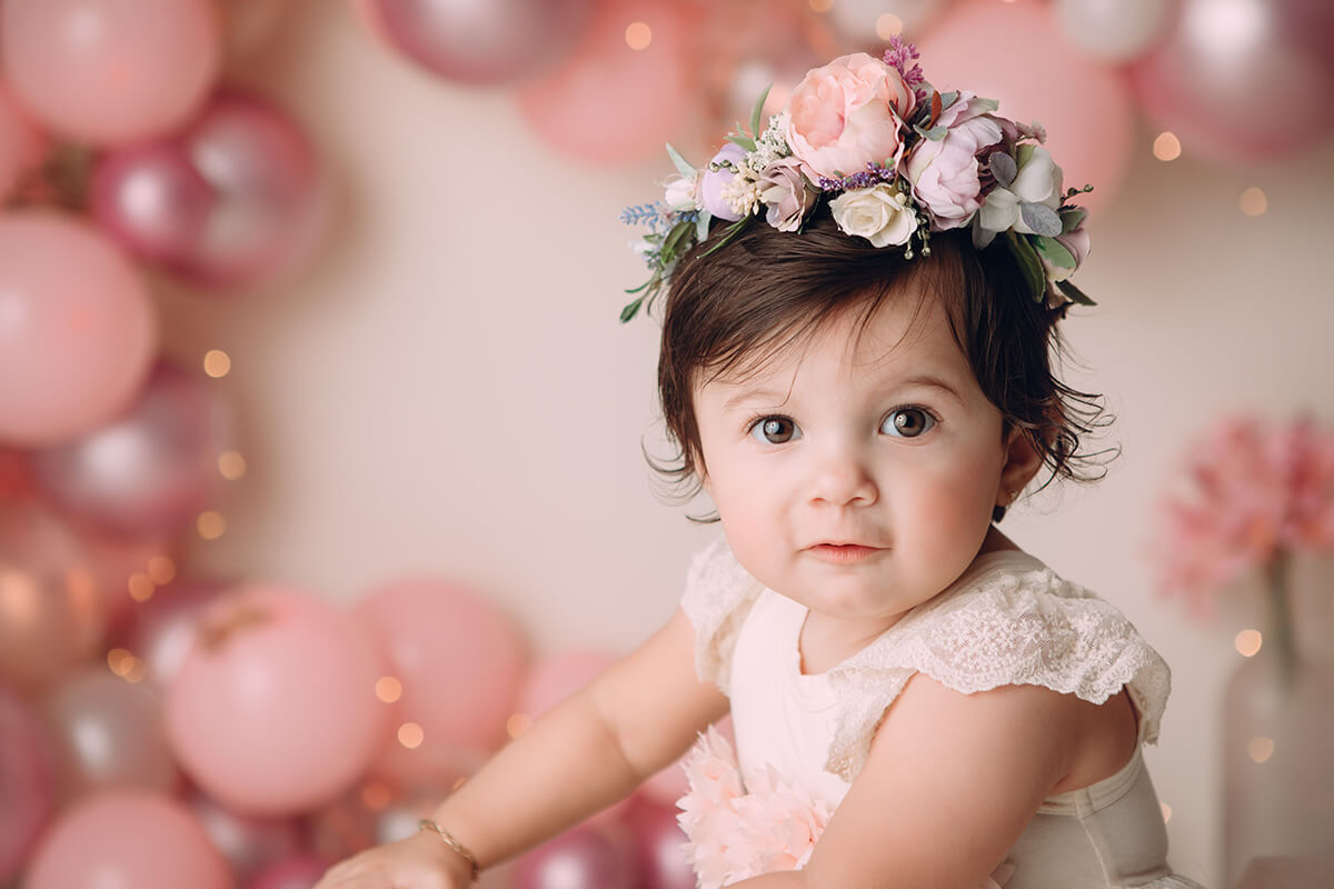 A closeup of a young toddler in a pink dress and matching floral hair piece in a studio