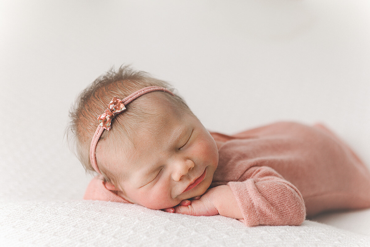 A sleeping newborn baby on her belly resting her head on her hands in a pink onesie after meeting doulas in Springfield, IL