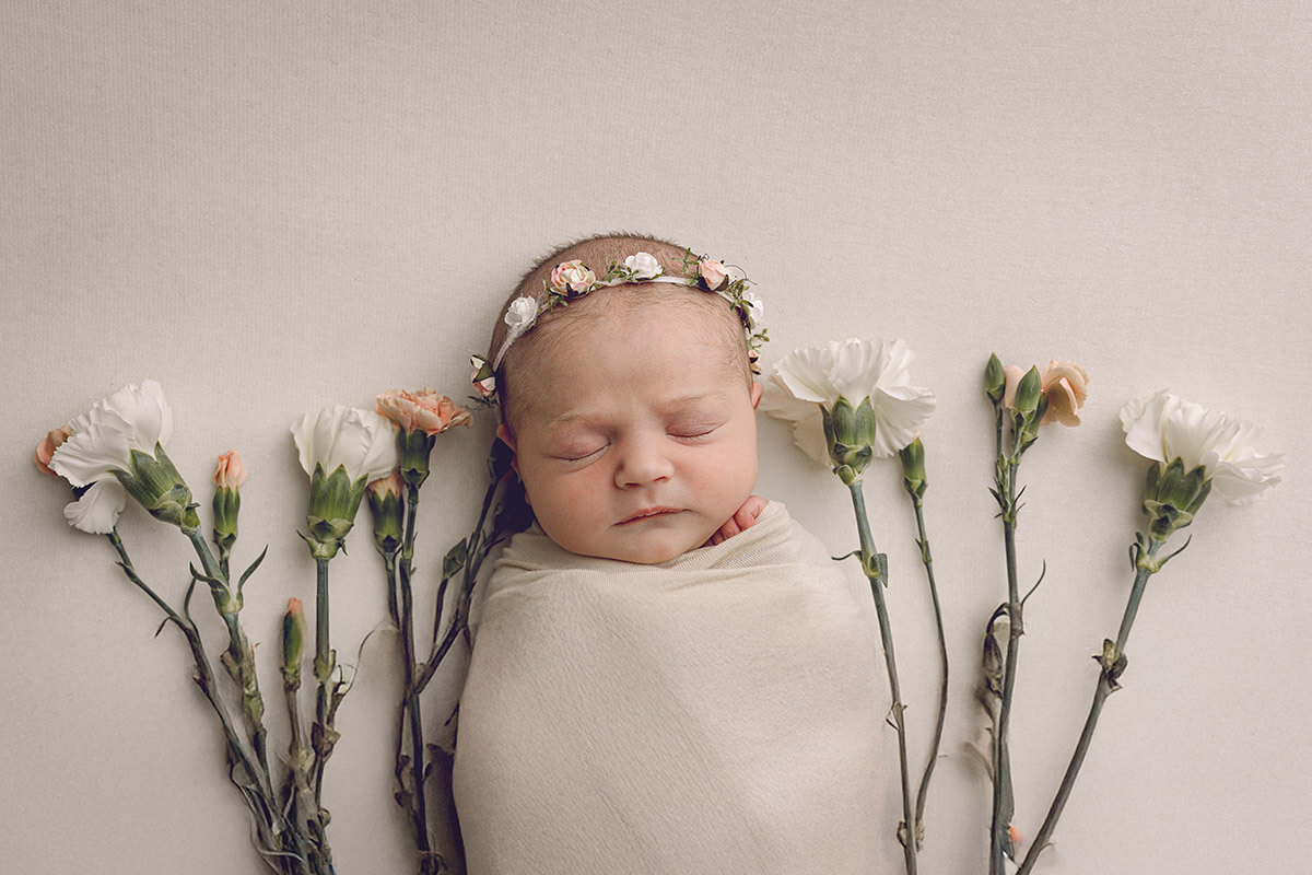 A sleeping newborn in a swaddle surrounded by white and pink flowers after meeting doulas in Springfield, IL