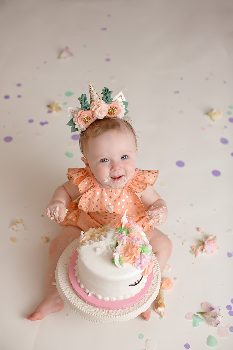 A happy infant plays in an orange dress covered in cake for first birthday cake smash after visiting indoor playgrounds in springfield il