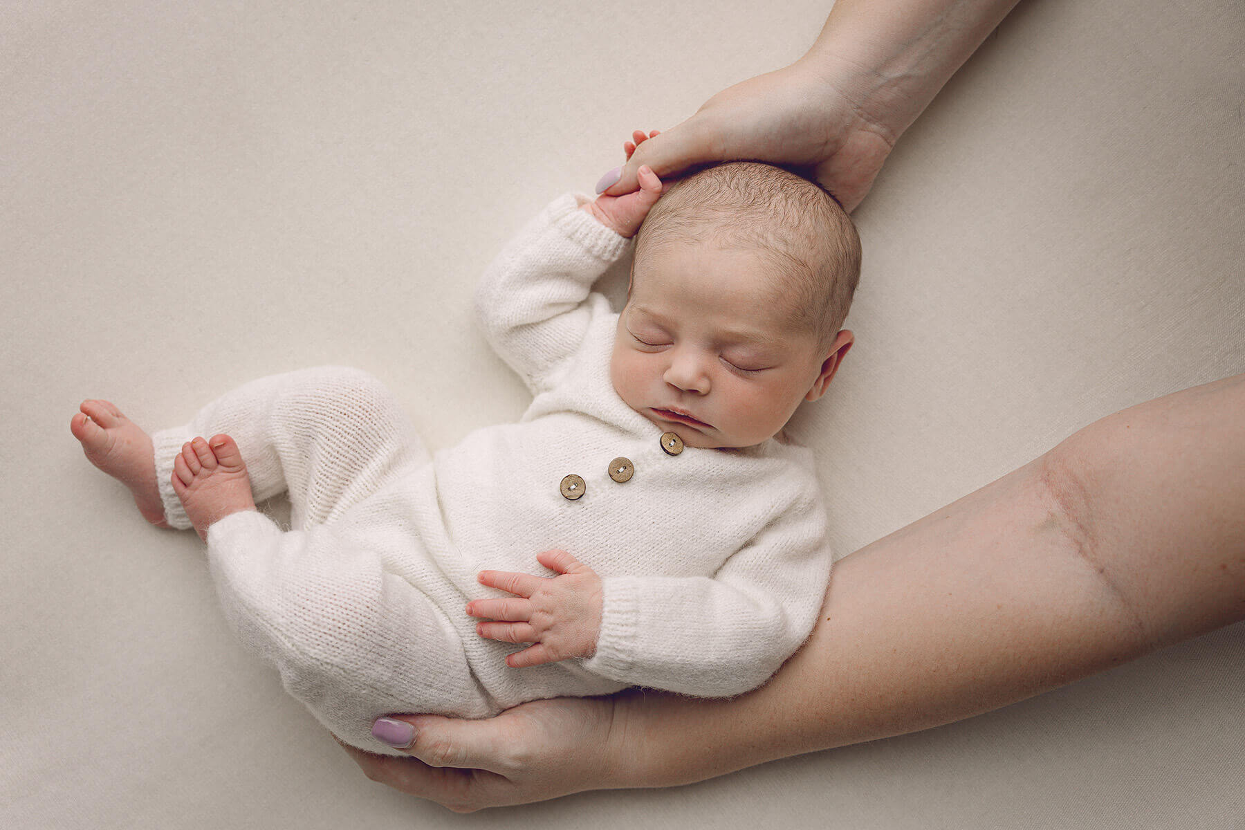 Mom cradles her sleeping newborn. with her hands while wearing a white onesie