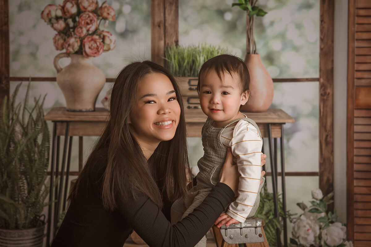 A happy mom holds her infant sitting on a tiny ladder in a studio