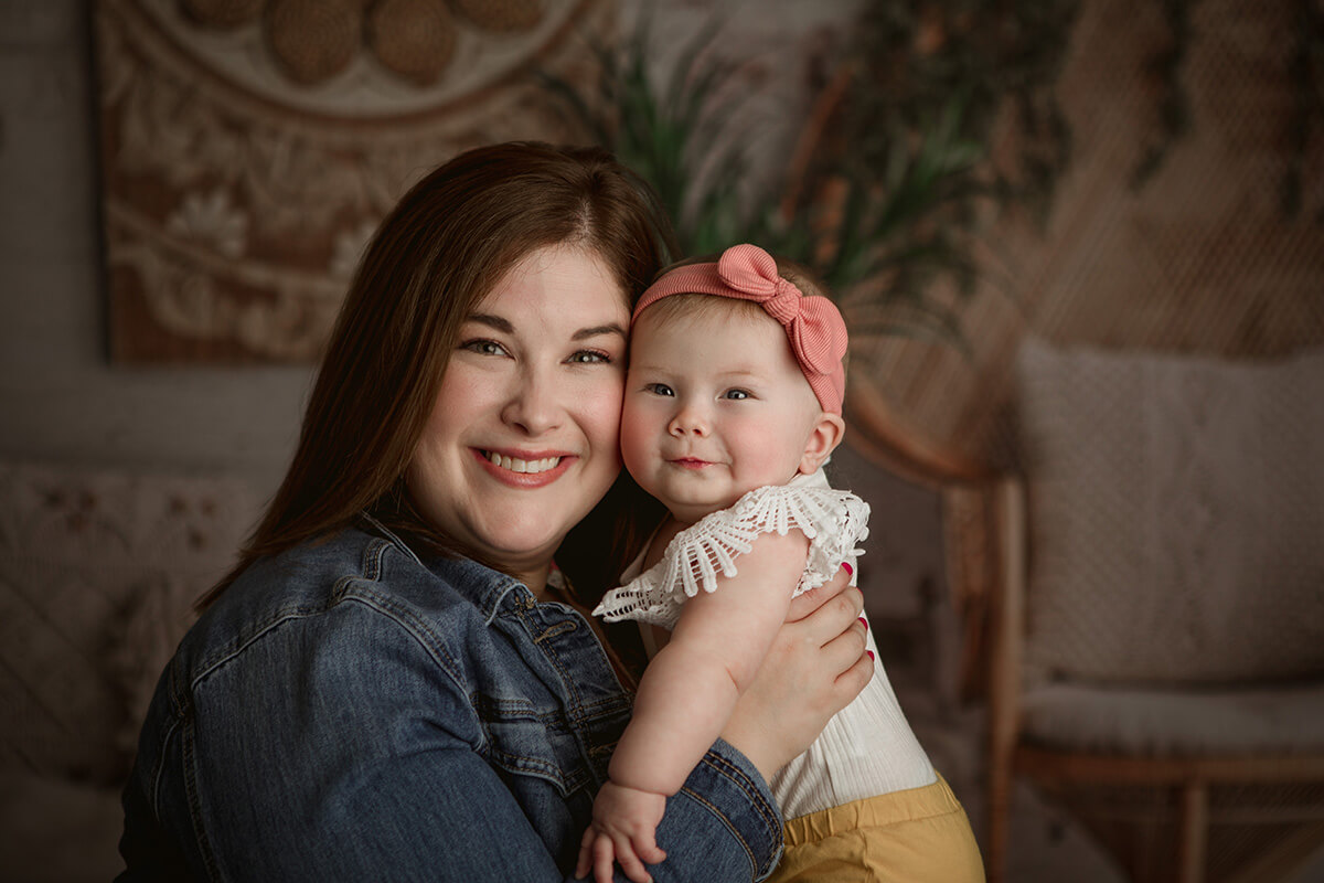 A happy baby held against mom's cheek in a pink headband after some fun mommy and me classes in Springfield, IL