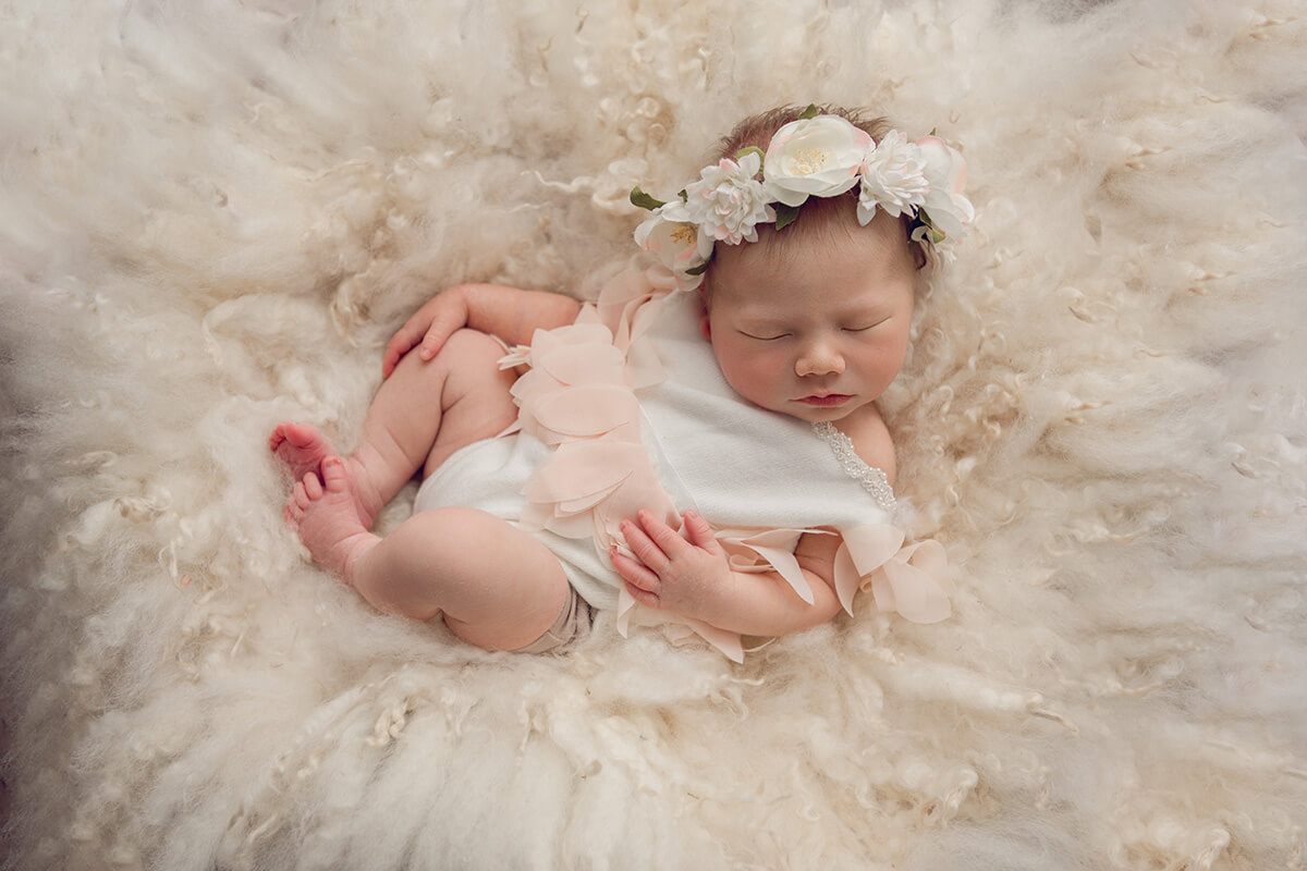 A sleeping baby girl in a white onesie and white floral headband after some newborn classes in Springfield, IL