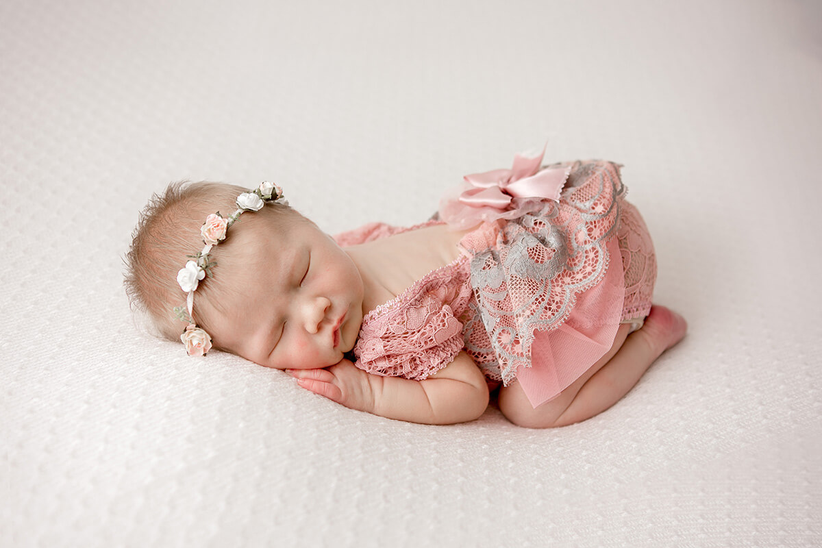 A newborn girl sleeps in froggy pose in a pink lace dress