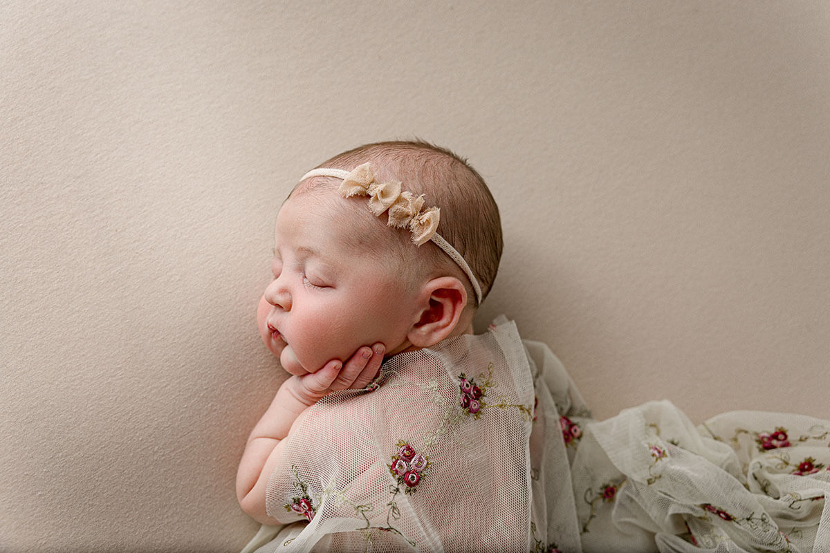 A sleeping newborn baby with a hand on her cheek under rose embroidered blanket after visiting pediatric chiropractors in springfield il