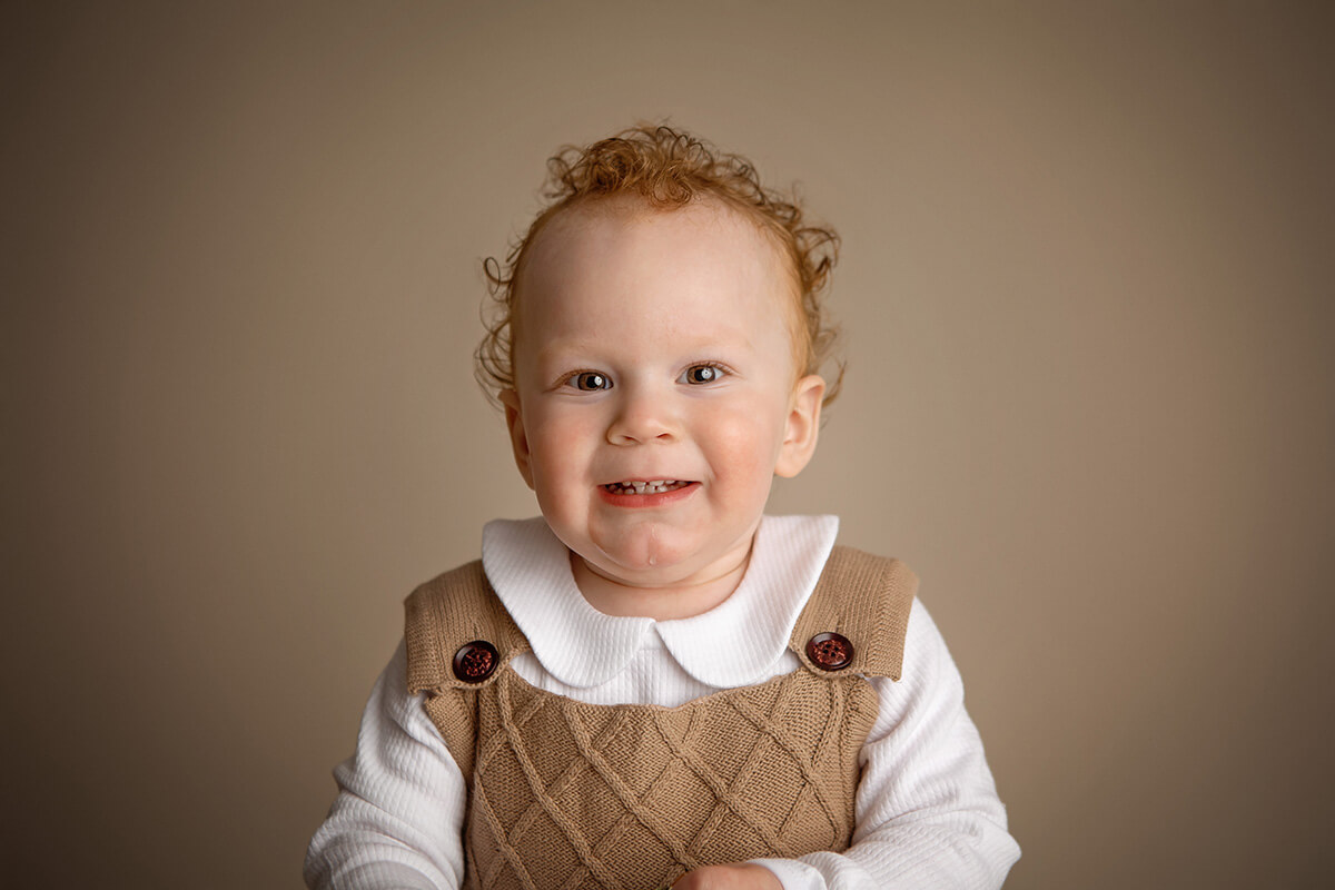 A toddler with red hair smiles while wearing brown knit overalls and a white shirt after visiting pediatric dentists in springfield il