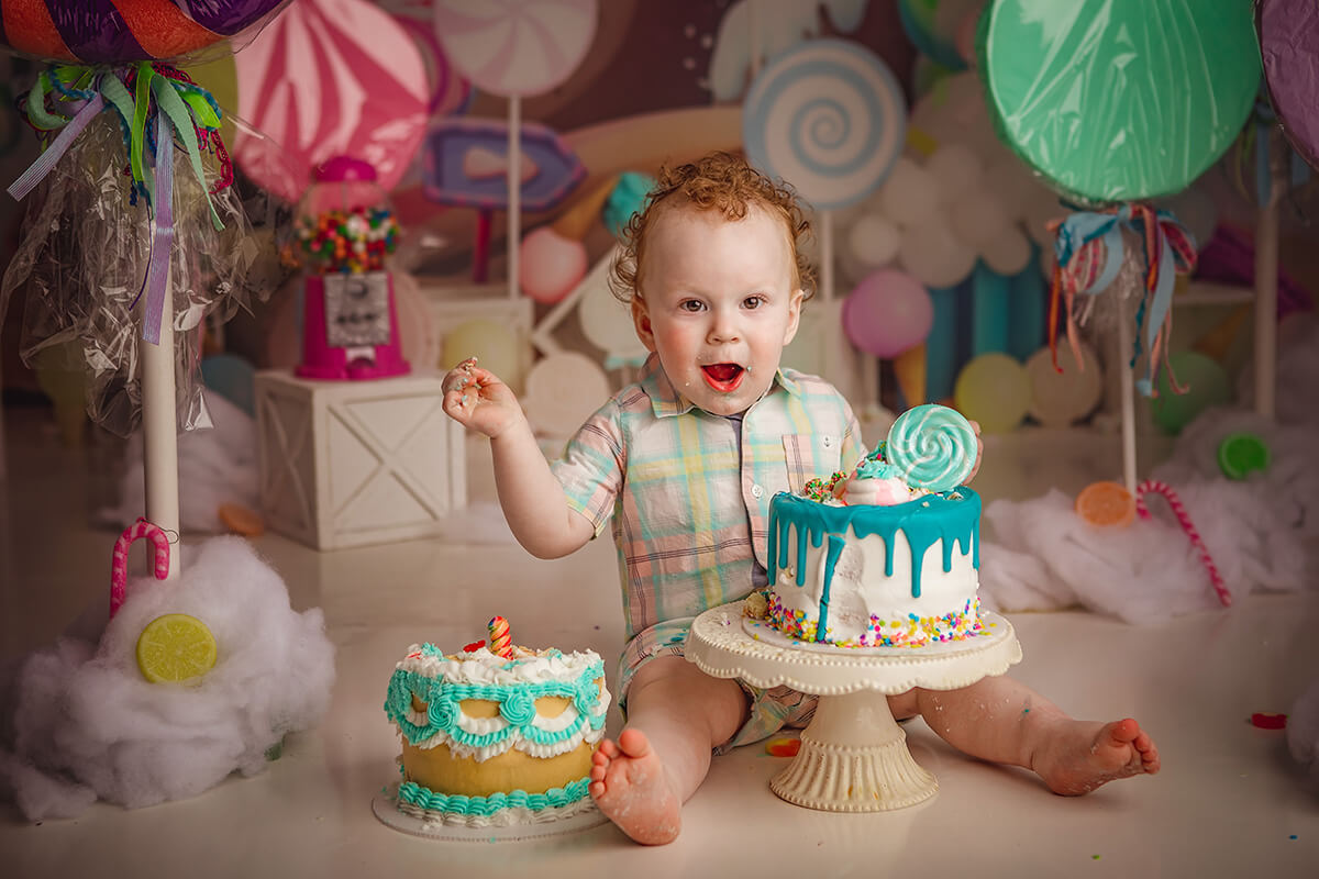 A happy toddler in a bright plaid outfit plays with a cake while sitting in a studio before visiting pediatric dentists in springfield il