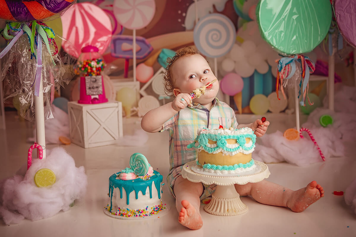 A happy toddler in a bright plaid outfit sits in a birthday themed studio eating a cake before visiting pediatric dentists in springfield il
