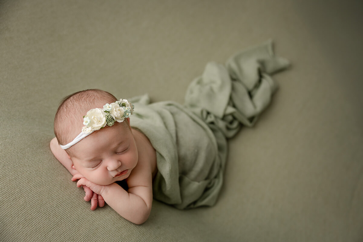 A newborn baby sleeps under a green blanket on her hands wearing a floral headband after visiting pediatricians in springfield il
