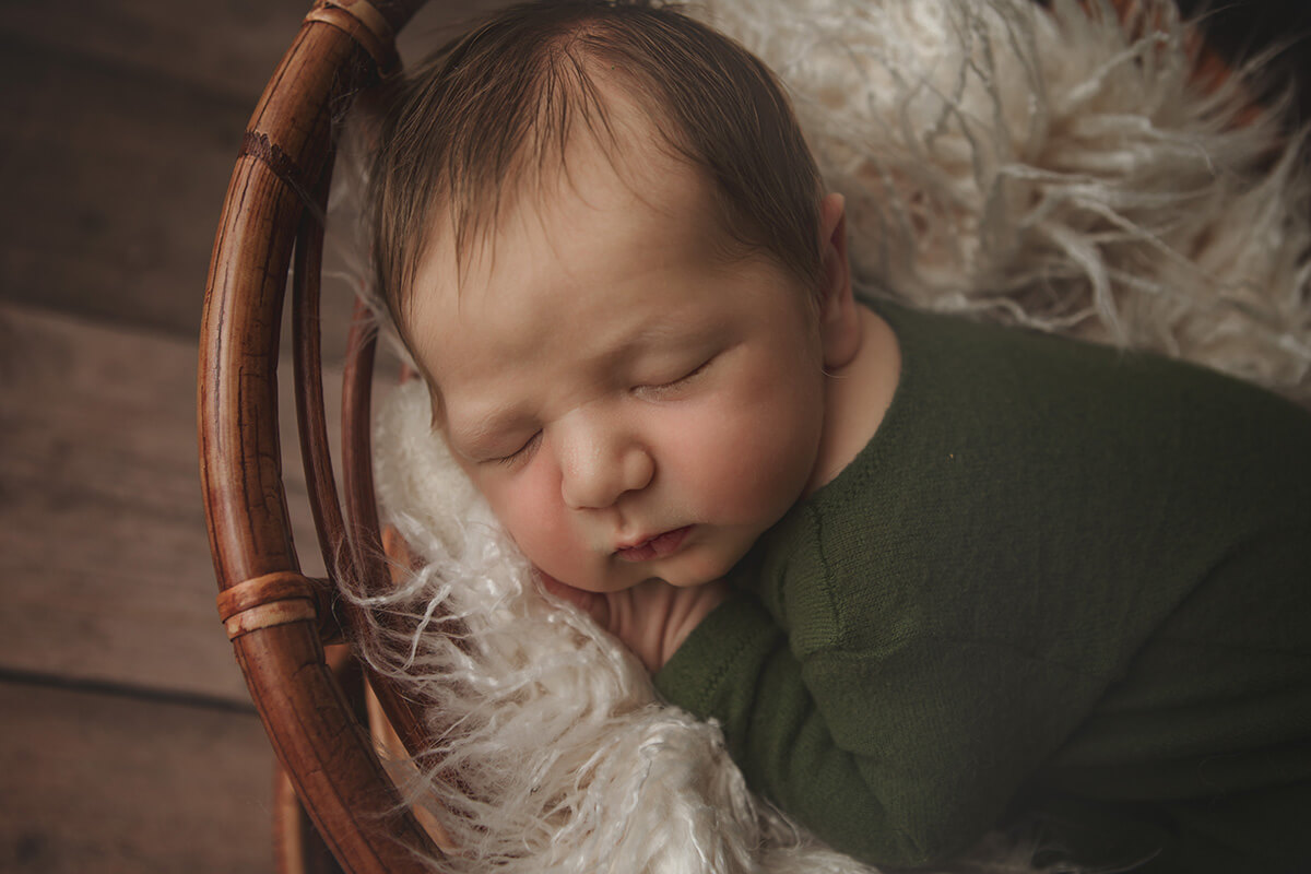 A newborn baby sleeps in a wicker bed in a green onesie on its side after visiting pediatricians in springfield il
