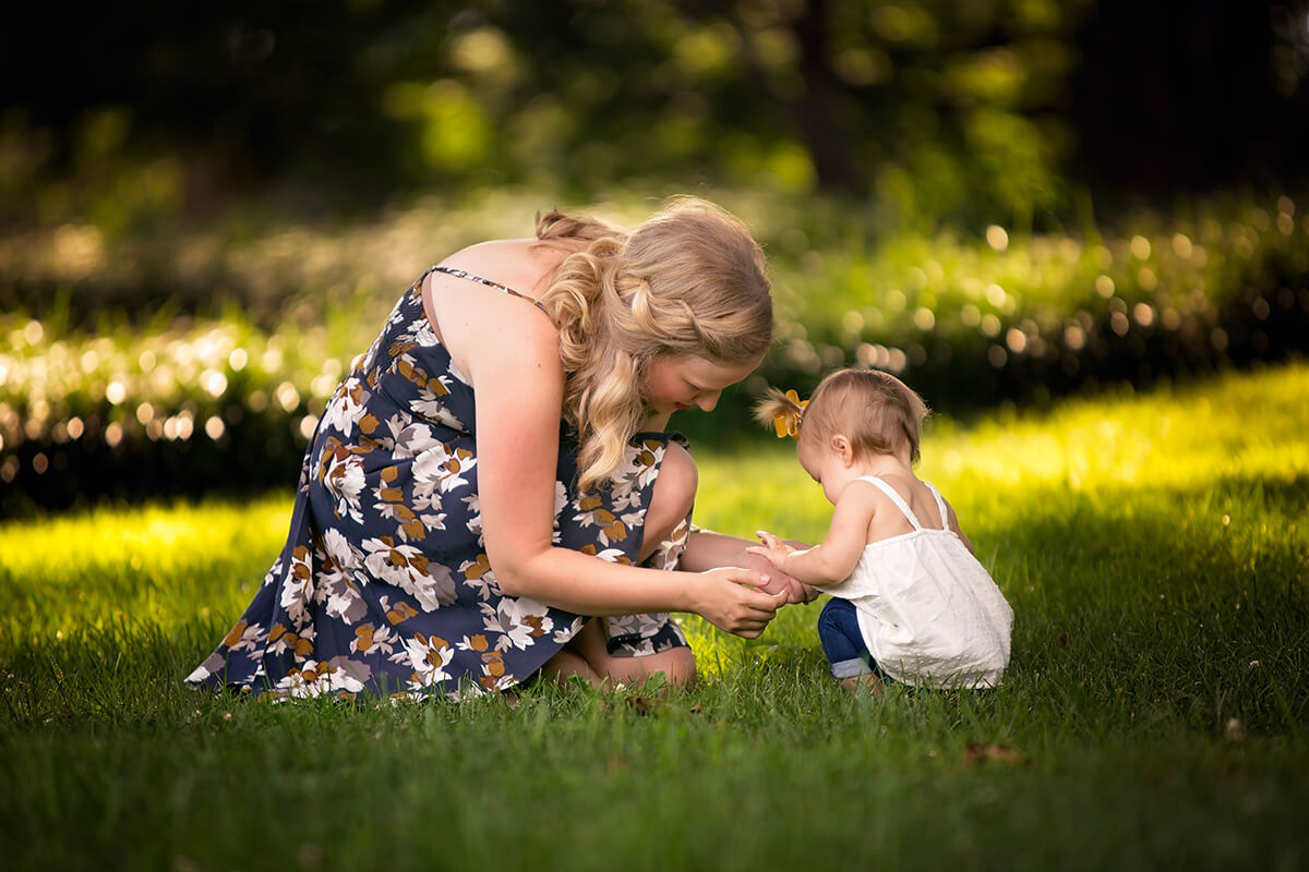 A happy mom plays in some grass with her toddler