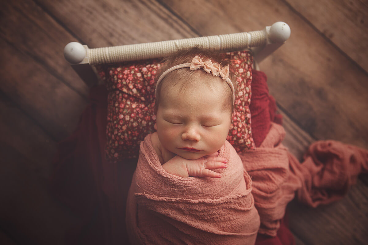A baby girl sleeps in a tiny bed wrapped in a pink swaddle