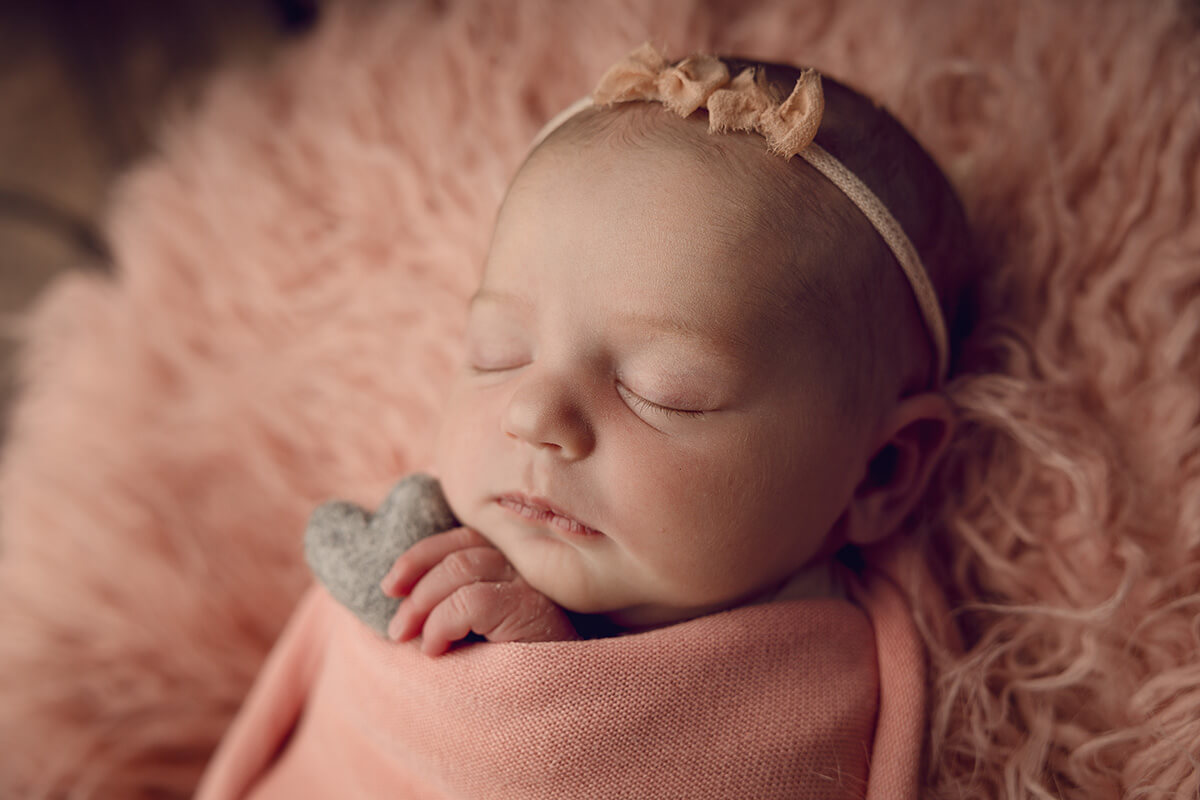 A newborn baby sleeping in a pink swaddle and headband on a matching shag blanket after meeting postpartum doulas in Springfield, IL