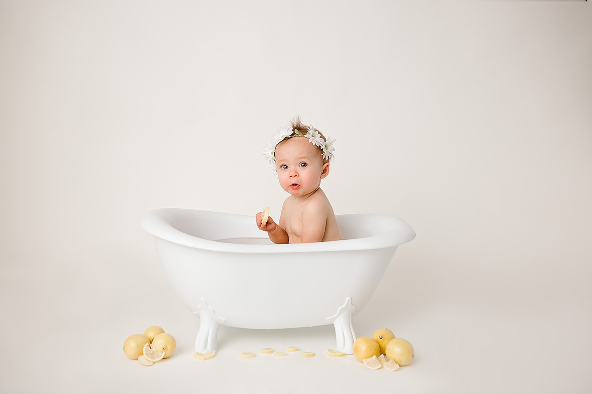 A baby makes a silly face while holding a lemon slice and sitting in a tiny bath tub in a studio after visiting splash pads in springfield il