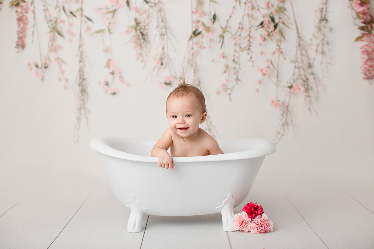 A happy baby sits in a tiny bath tub in a studio smiling after visiting splash pads in springfield il