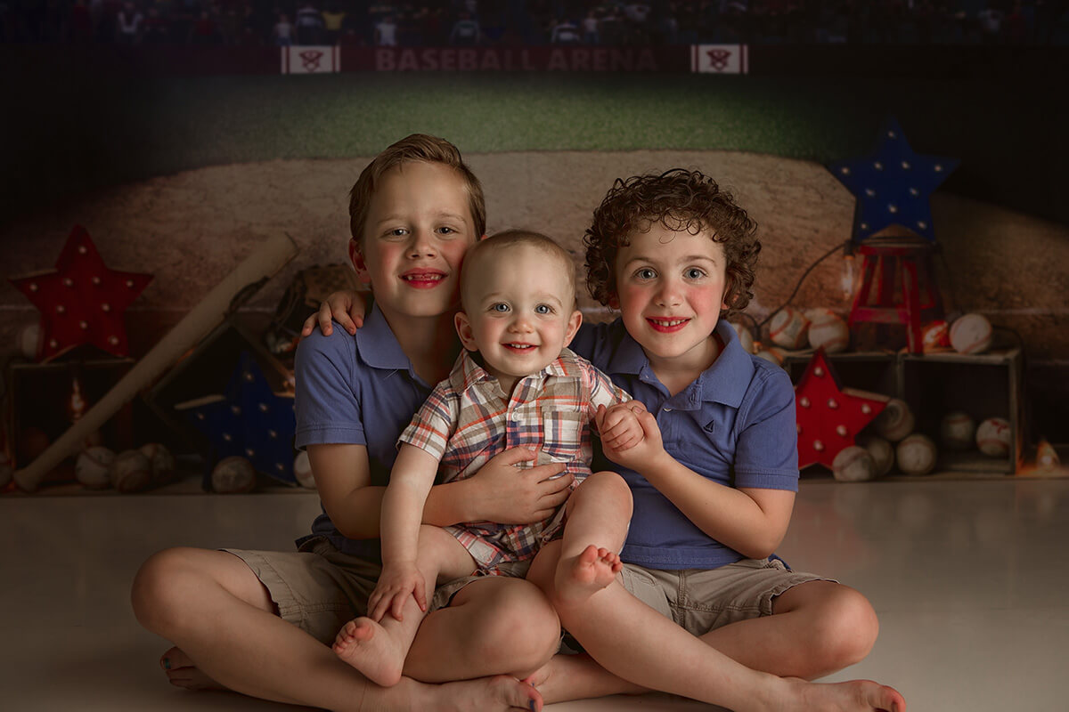 Two young brothers in matching blue polos sit with their baby brother in their laps in a studio