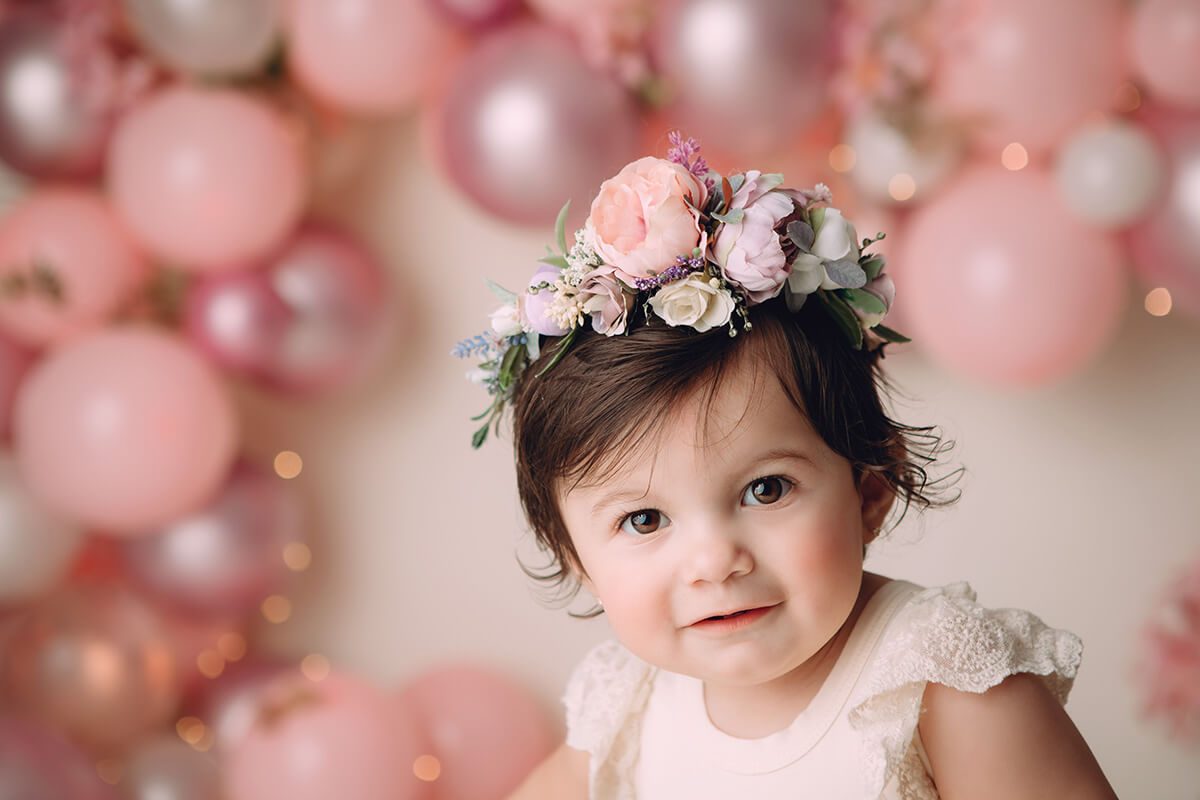 A closeup of a baby girl with a flower hair piece in a pink dress