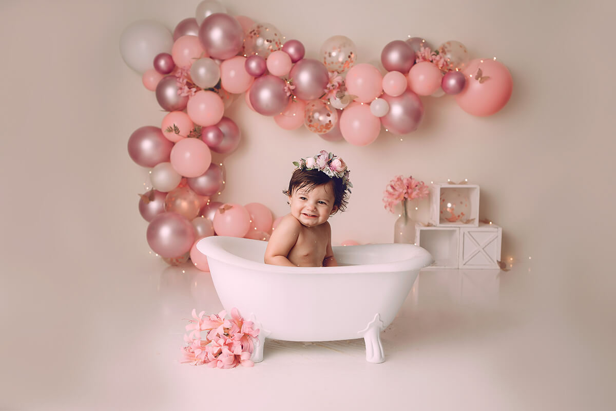 A baby girl in a bathrub giggling with Balloons by Gabi on the wall behind her