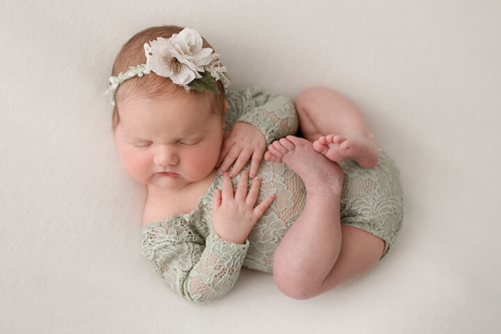A newborn baby sleeping in a green lace onesie with white flower headband