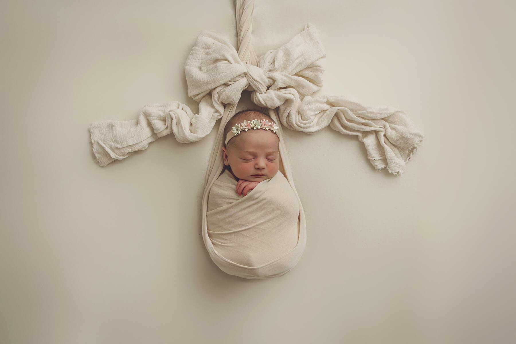 A newborn baby sleeps in a white swaddle under a bow with flower headband after using baby shower venues in Springfield, IL