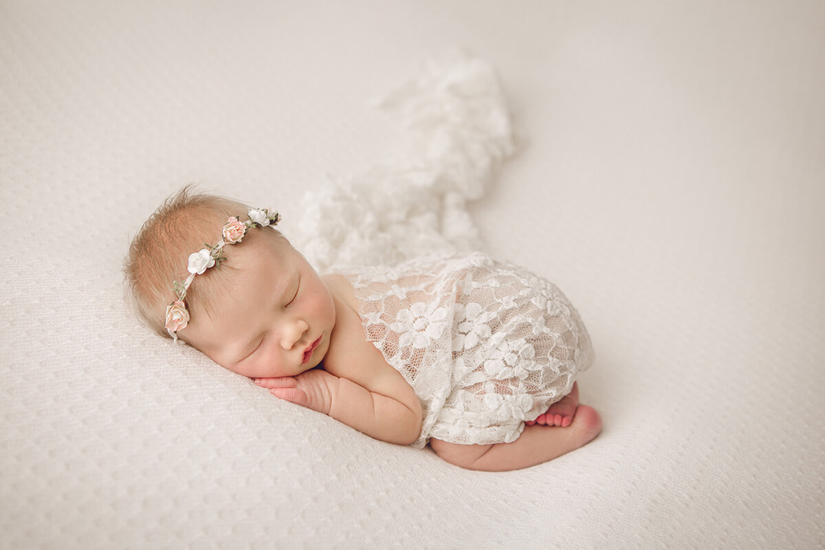 A newborn baby sleeps in froggy pose under a white lace blanket after using baby shower venues in Springfield, IL