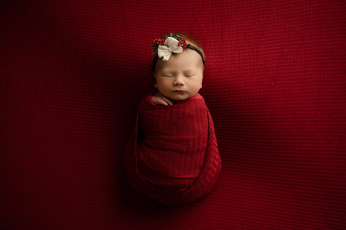 A sleeping newborn baby in a red swaddle and matching headband