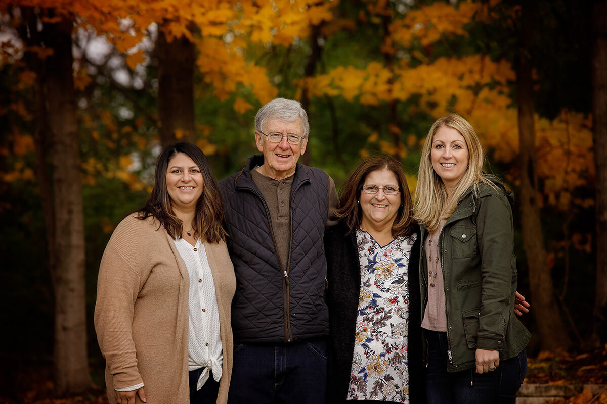A mom and dad smile with their adult daughters in a park