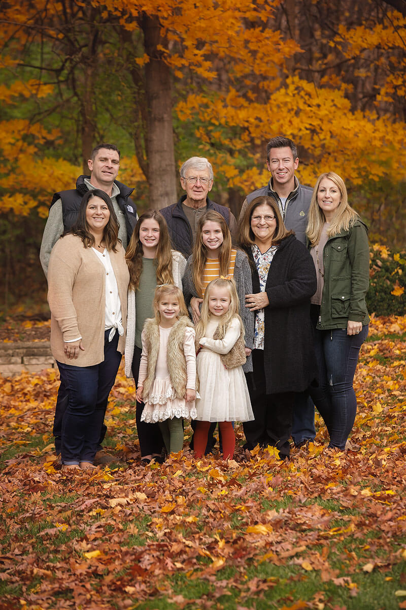 A large extended family stand smiling together in a park in fall