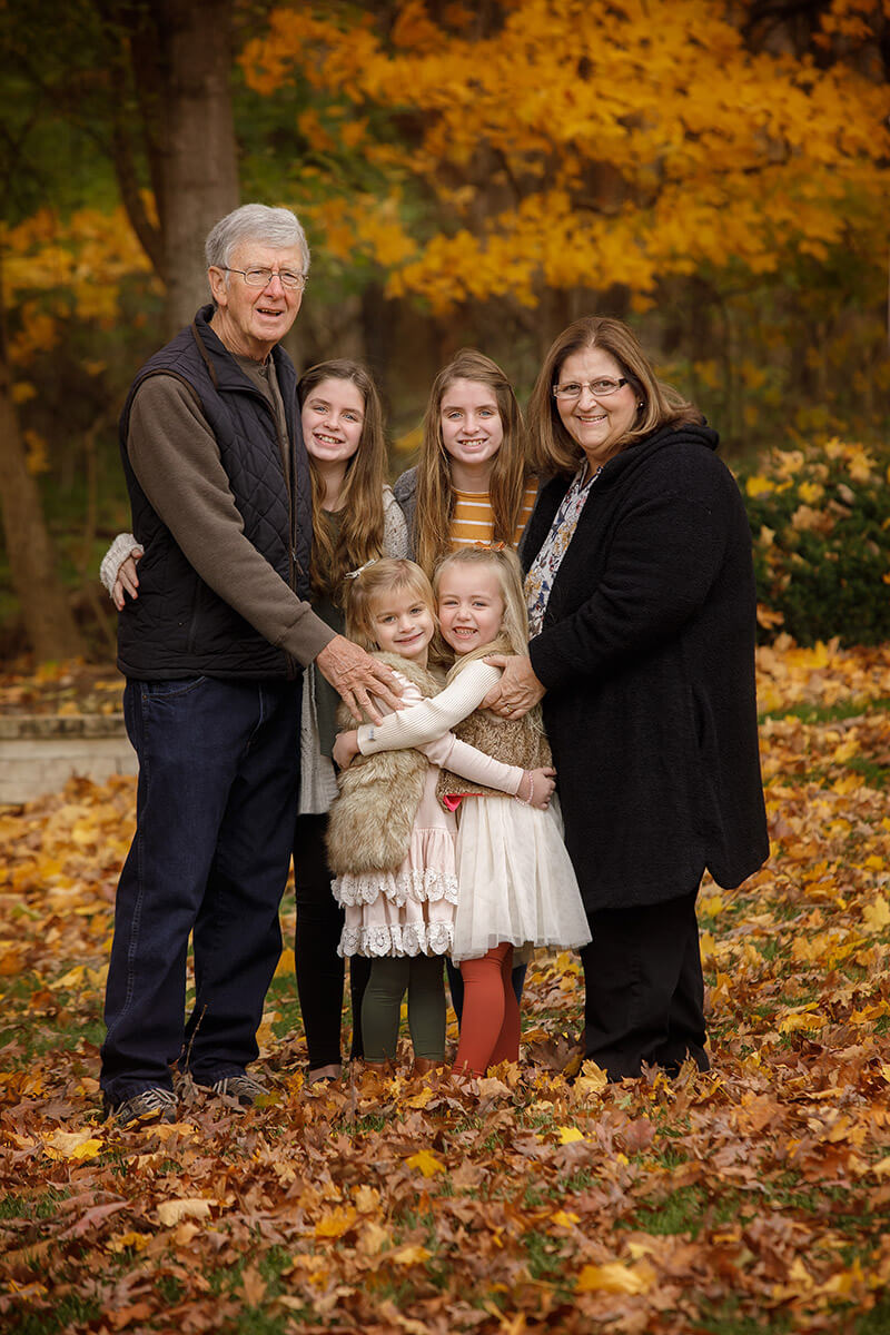 Grandma and grandpa stand hugging their four granddaughters in a park in fall during some family activities in Springfield, IL