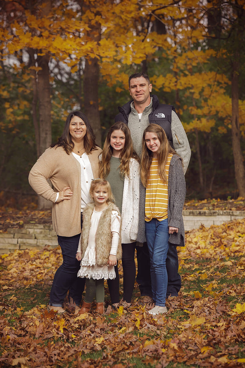 A mom and dad stand smiling with their three young daughters in a park in fall in sweaters during some family activities in Springfield, IL