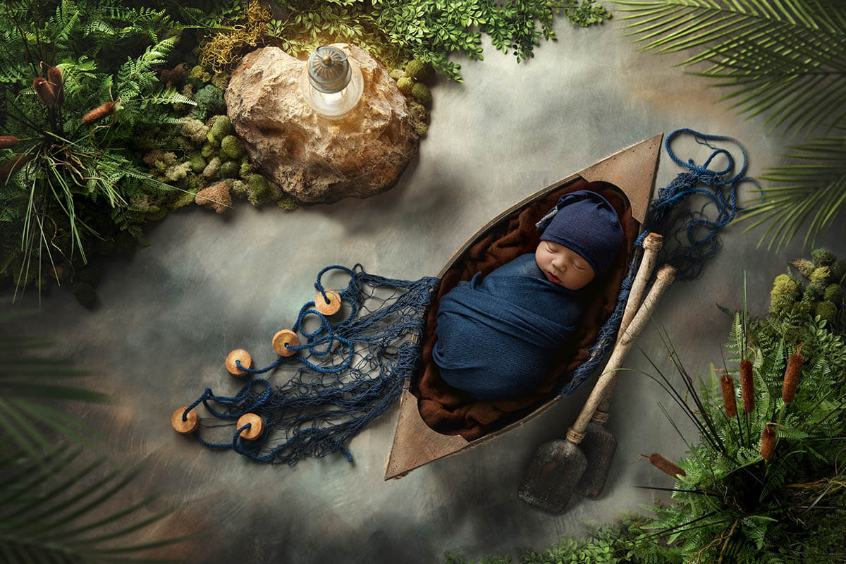 A sleeping newborn baby in a blue swaddle in a fishing canoe in the water