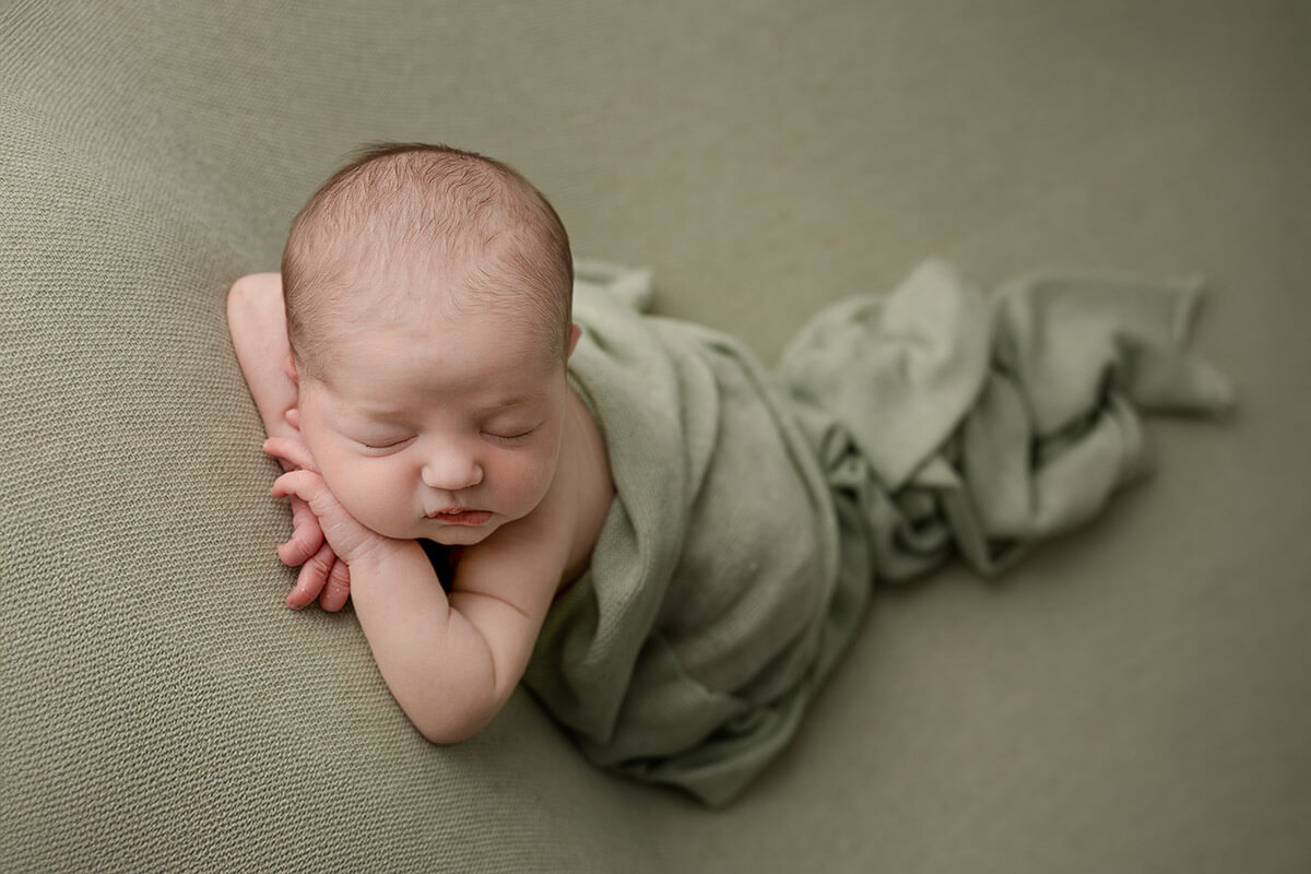 A newborn baby sleeps in froggy pose under a green blanket after using a midwife in Springfield, IL