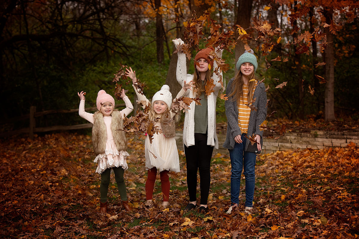 A group of cousins in sweaters and beanies tossing fallen leaves in the air