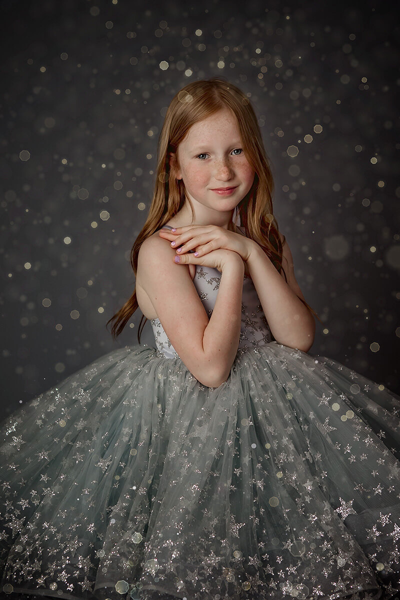 A young girl stands in a studio wearing a silver gown with shiny stars with hands on her shoulder after visiting preschools in Springfield, IL