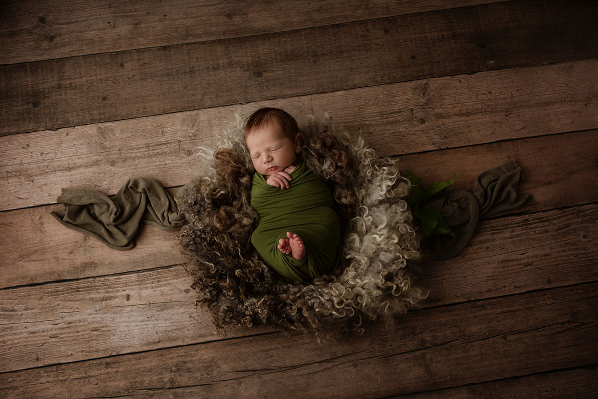 An infant sleeps in a green onesie on a fuzzy blanket on wood floor after a 3d ultrasound in Springfield, IL