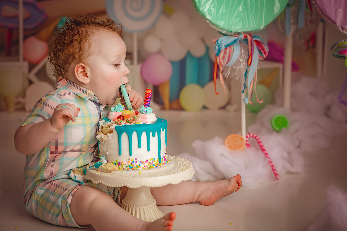 A baby boy in a plaid onesie takes a bite out of a cookie cake topped for his birthday