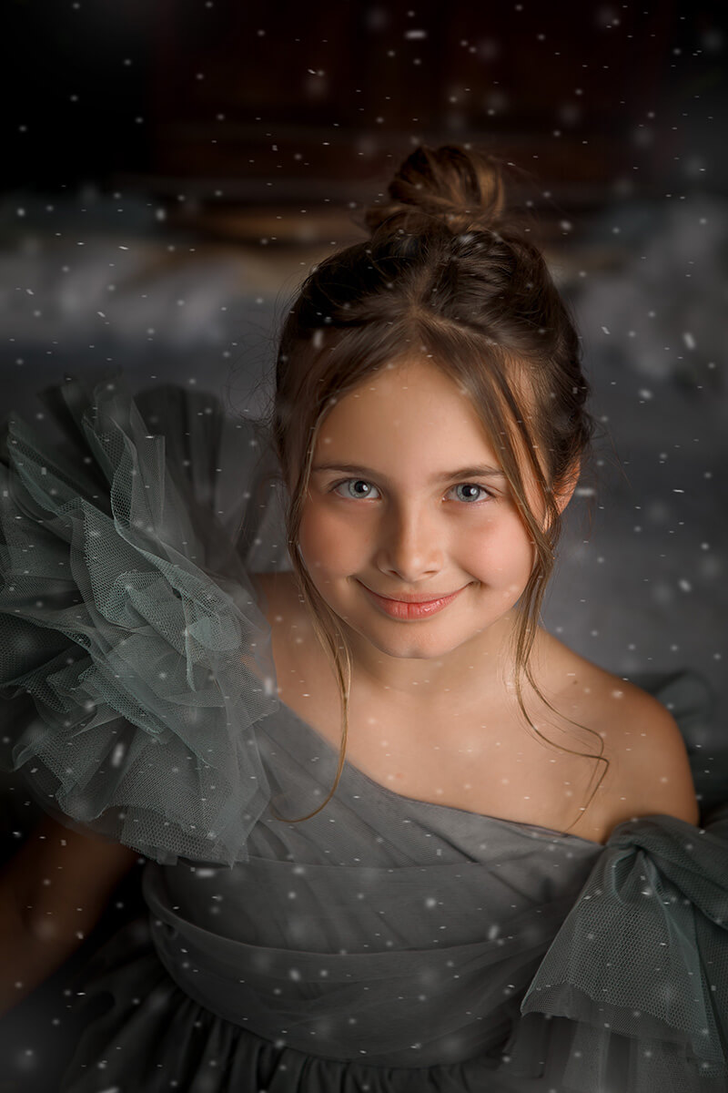 A young girl smiles in the snow in a large grey tulle gown