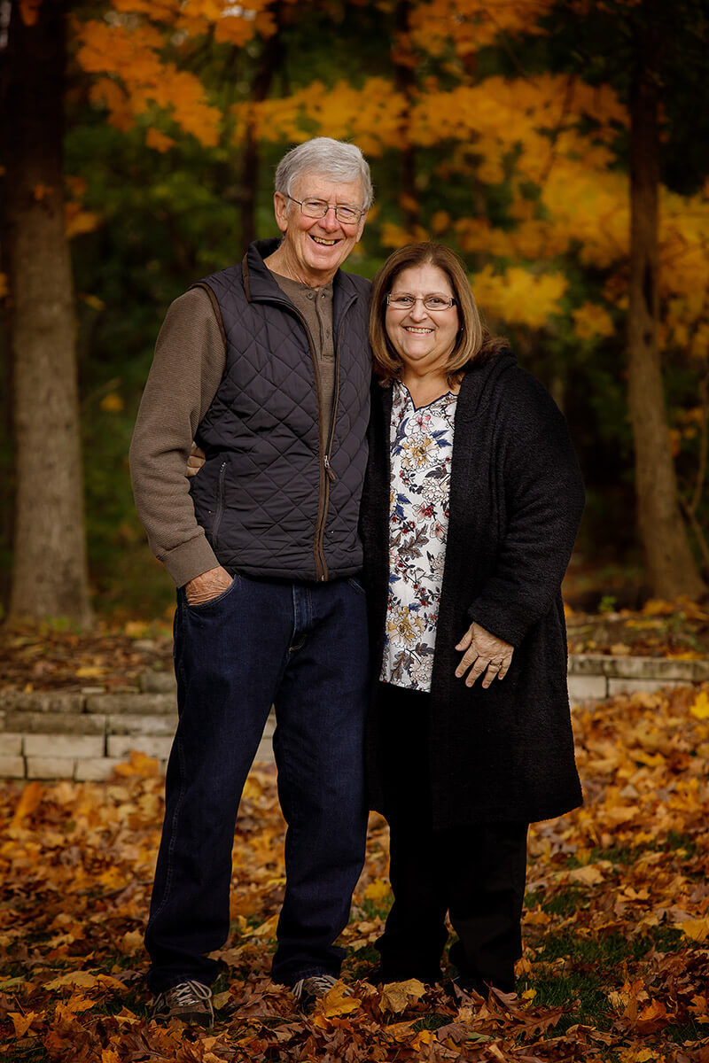 Happy grandparents stand smiling with arms around each other in a fall lawn before visiting fall festivals in Springfield, IL