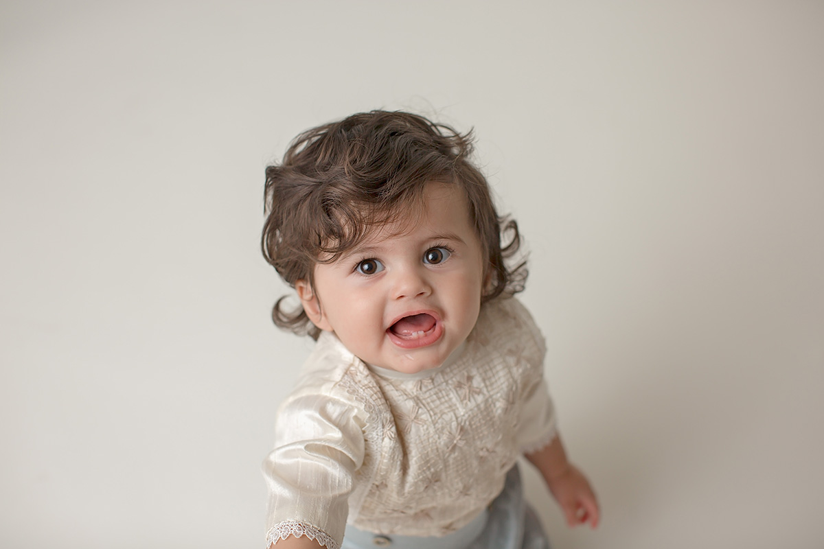 A happy baby talks while wearing an off white blouse in a studio