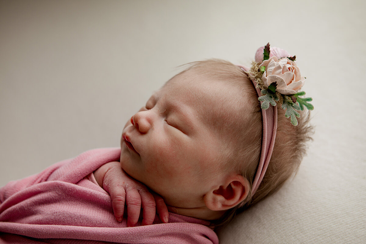Details of a sleeping newborn baby's face in a pink flower headband