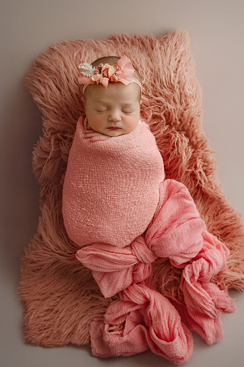 A newborn baby girl sleeps in a pink swaddle with large bow on the bottom and her head after finding an obgyn in Springfield, IL