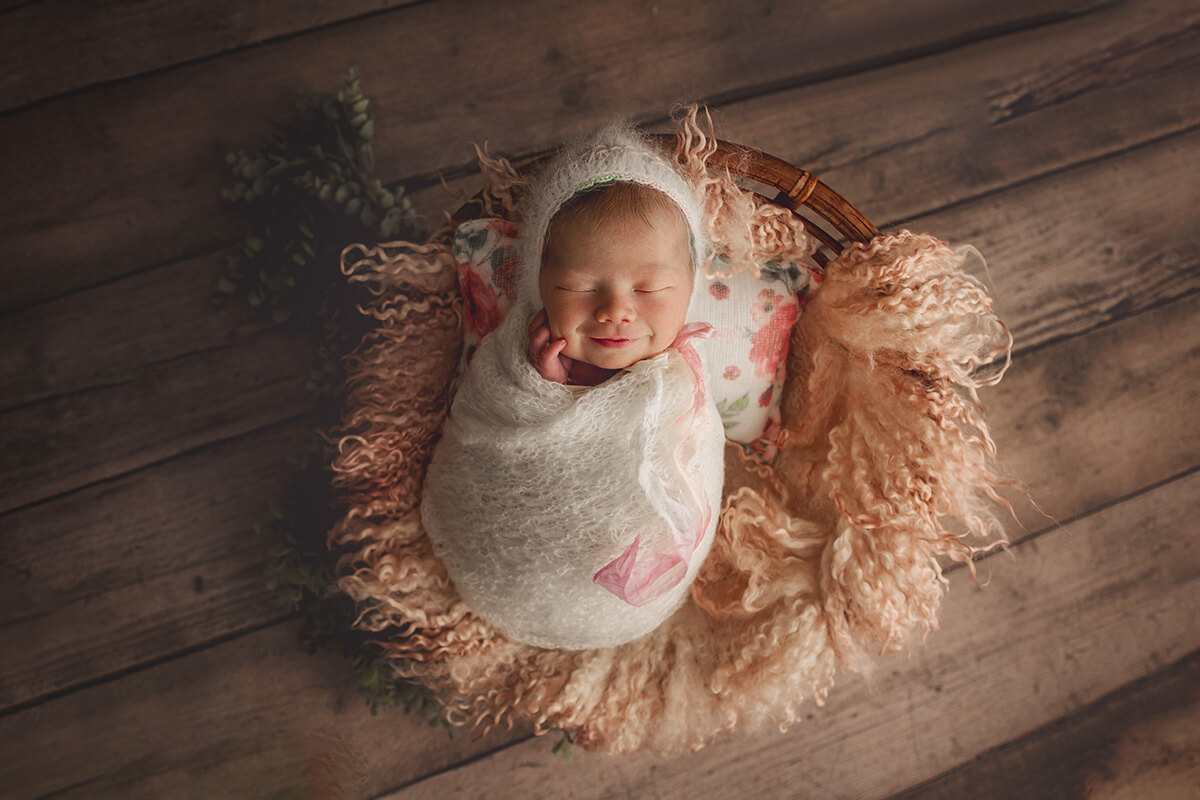 A happy newborn in a white swaddle in a wicker basket