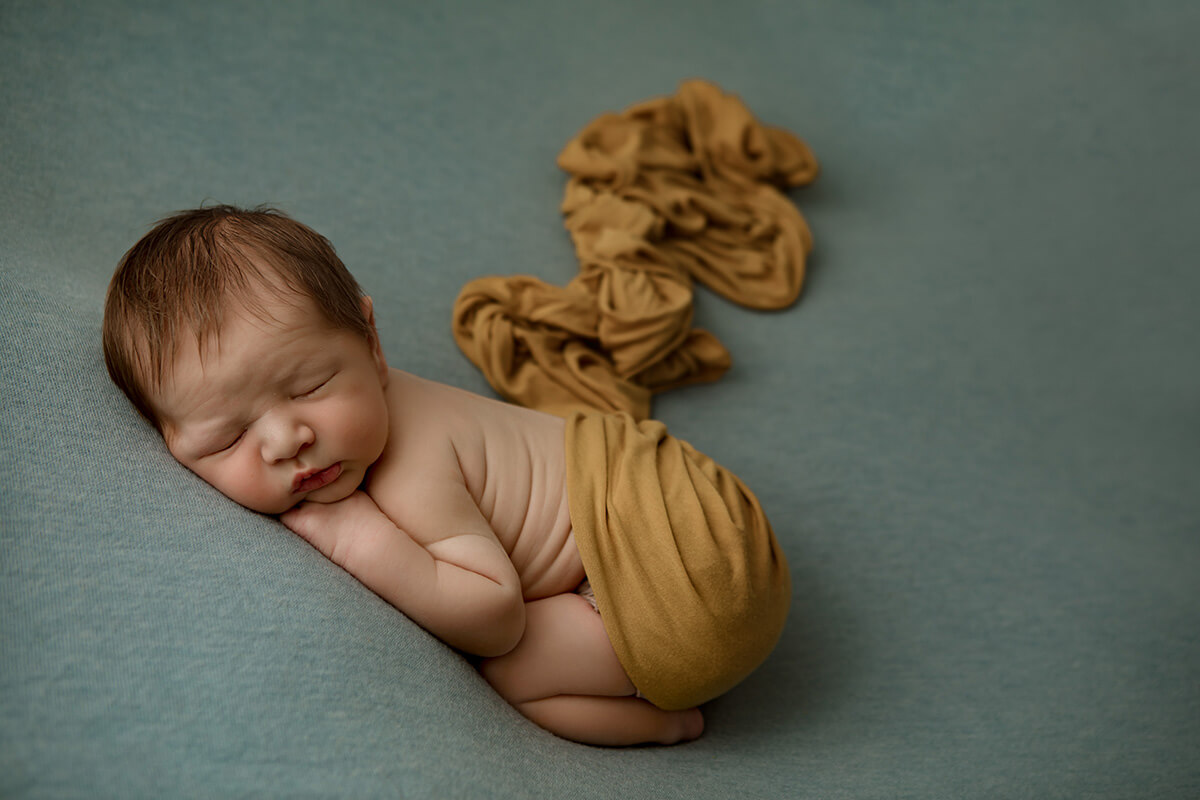 A sleeping newborn under an orange blanket in froggy pose in a studio after some parenting classes in springfield, il